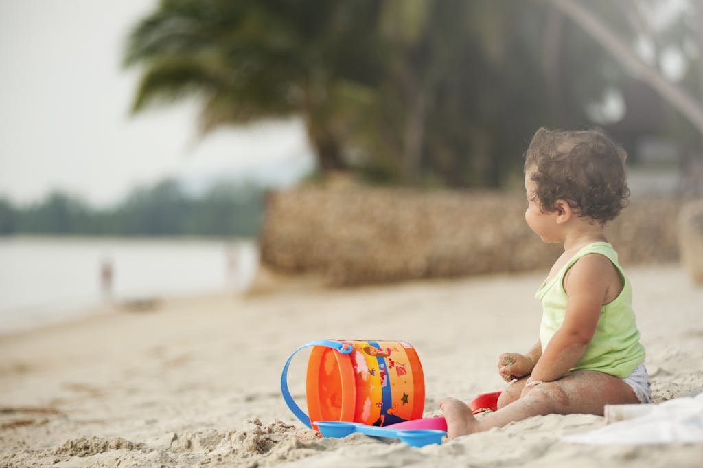 A young child plays happily with a bucket and sand on a tropical beach in Thailand.