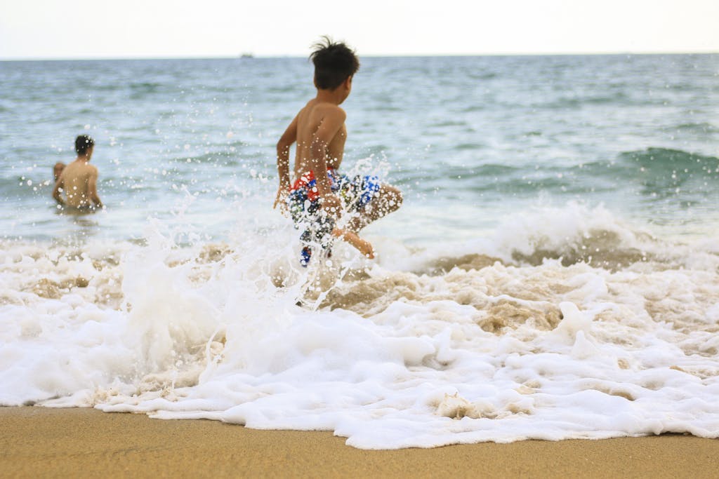 Two children enjoying playful moments in ocean waves on a sunny beach day.