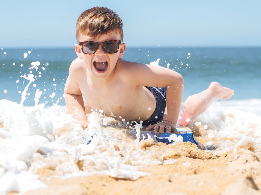 Young boy in sunglasses rides ocean waves on a beach with bright joy.